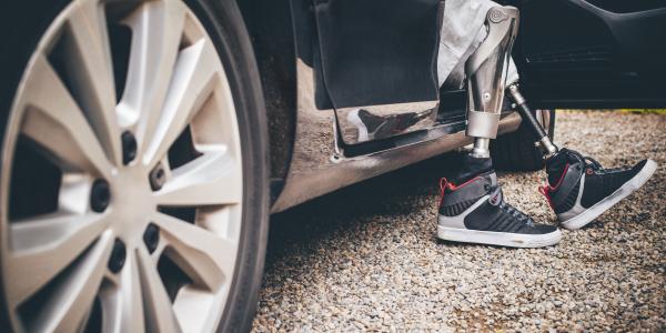 Man with prosthetic legs getting out of the drivers seat of a car.