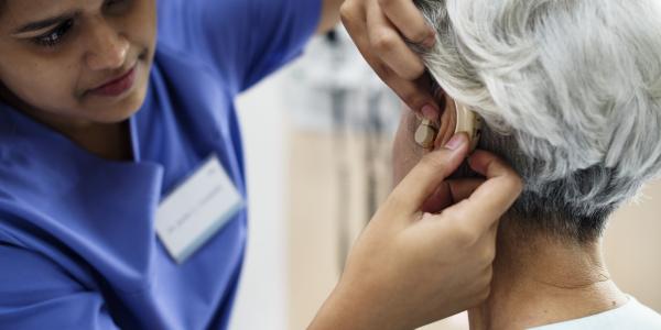 An elderly person with hearing aid being assisted by a care provider.