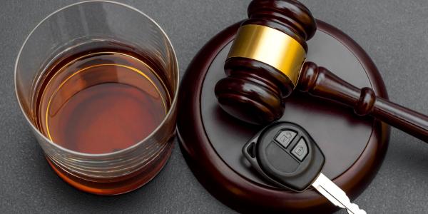 Judge's gavel with car key and glass of whiskey on black background.