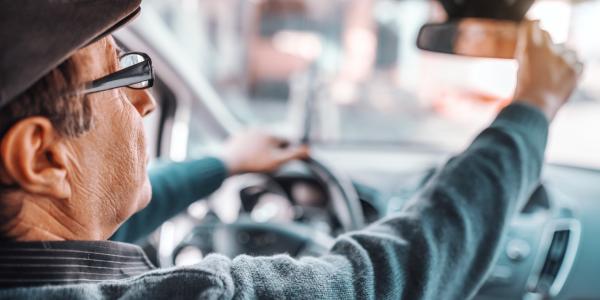 Mature person with hat and eyeglasses adjusting rear mirror while sitting in their car.