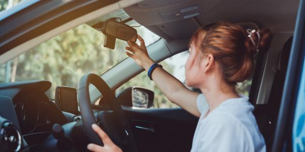 Person adjusts the cars rearview mirror in interior before starting to drive.