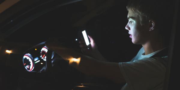 Distracted teenager driving a car with a cell phone in their hand. 